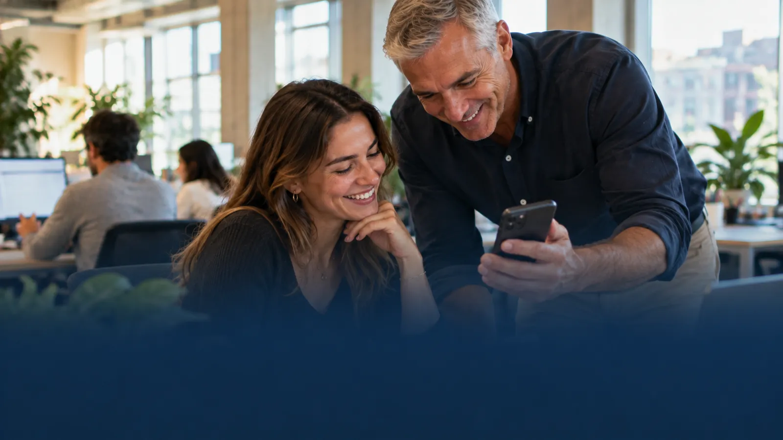Two coworkers smiling at a phone in a bright office